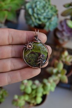 a person holding a pendant in their hand near some succulents and potted plants