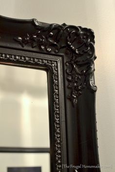 an ornate black framed mirror hanging on the wall next to a white wall with a reflection in it