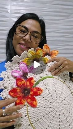 a woman is holding a crocheted hat with flowers on it