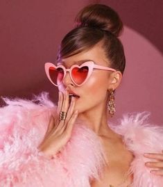 a woman wearing pink heart shaped sunglasses with her hands on her face and holding her hand up to her mouth