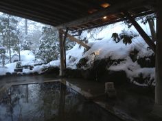 snow is covering the ground and rocks under a covered in area with a hot tub