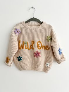 a child's sweater with flowers and the word hello on it hanging from a hanger