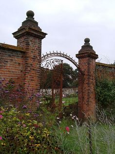 an old brick gate is surrounded by wildflowers and other plants in the foreground