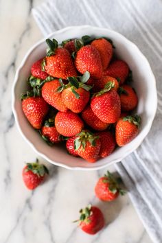 a white bowl filled with strawberries on top of a marble countertop next to a towel