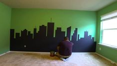 a man sitting on the floor in front of a wall with a cityscape painted on it