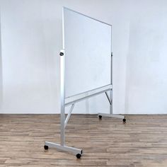 a white board sitting on top of a wooden floor next to a metal stand with wheels