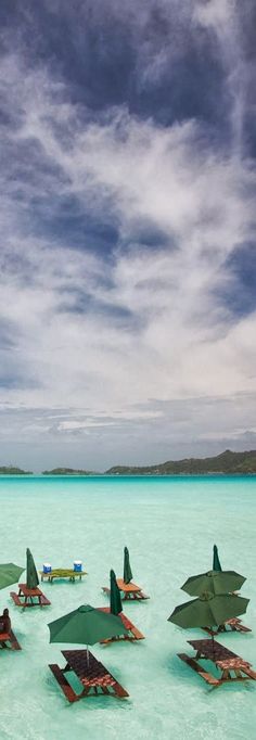 many umbrellas and lounge chairs are in the shallow blue water on an ocean beach