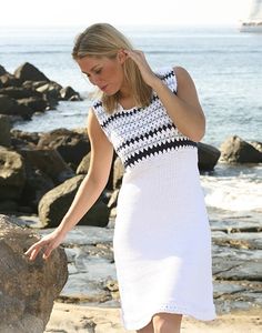 a woman in a white dress is standing on the rocks by the ocean and touching her hair