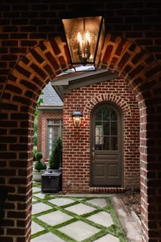 an archway leading into a brick house with grass growing on the ground and lights hanging from it