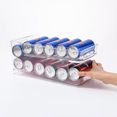 a person is holding a tray with many cans and batteries on it while another holds a bottle in the other hand