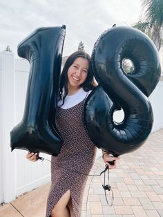 a woman holding two large black balloons in the shape of the number twenty eight,