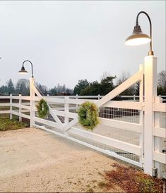 a white fence with wreaths on it and two lights hanging from the top one