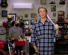 a man holding a baseball bat standing in a garage with other men and motorcycles behind him