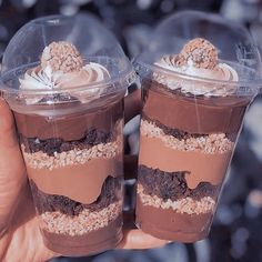 two desserts in plastic cups being held by someone