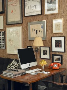 a desk with a computer on top of it in front of pictures and framed photos