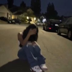 a person sitting on the ground in front of some cars at night with their hands over their face