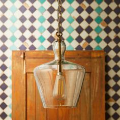 a glass light hanging from a chain in front of a wall with colorful tiles on it