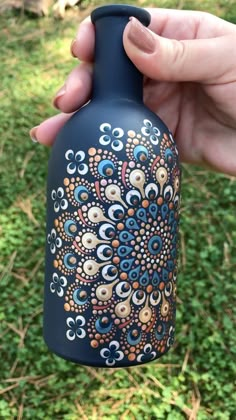 a hand holding a blue vase with an intricate design on the outside, and green grass in the background