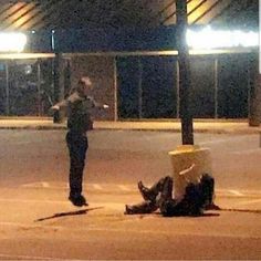 a person laying on the ground in front of a parking lot with a police officer standing next to it