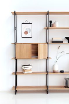 a book shelf with books, vases and other items on it in front of a white wall