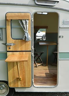 an old camper trailer with its door open and the table in the doorway is next to it