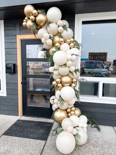 a tall white and gold balloon arch with greenery on the top, in front of a building