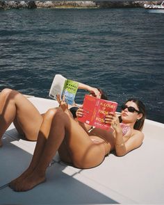 a woman laying on the back of a boat reading a book with her legs crossed