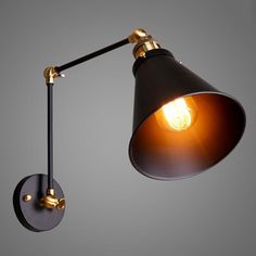 an old fashioned wall light with a black and gold shade on the side, against a gray background