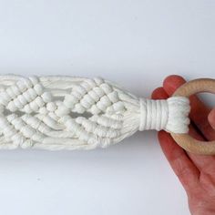 a hand holding a wooden ring with white rope on it and an object in the background