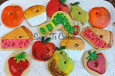 some very pretty decorated cookies on a white plate with strawberries, apples, and cupcakes