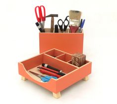 an orange desk organizer with scissors, pencils and other office supplies in it on a white background