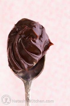 a spoon filled with chocolate frosting on top of a pink wallpapered background