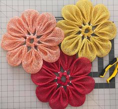 three different colored flowers sitting on top of a cutting board next to scissors and yarn