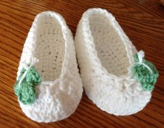 a pair of crocheted baby shoes on a wooden floor with a green bow