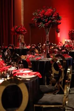 a room filled with tables covered in black and red table cloths next to tall centerpieces