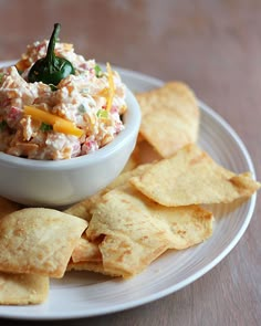 a white plate topped with chips and a bowl filled with coleslaw dip surrounded by tortilla chips