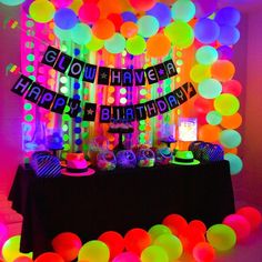 a birthday party with neon colored balloons and streamers on the wall, along with a black table cloth that says glow have happy birthday