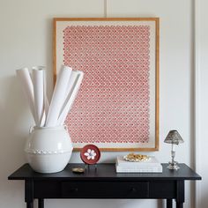 a black table topped with a white vase filled with flowers next to a framed art piece