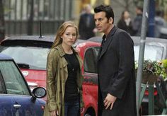 a man and woman standing next to each other in front of parked cars on a city street