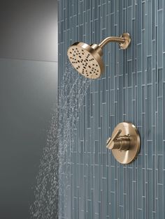 the shower head is spraying water from it's faucet, which is attached to a tiled wall