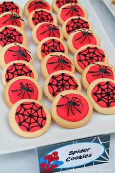 cookies decorated with red and black spider webs are on a white plate next to a sign that says spider cookies