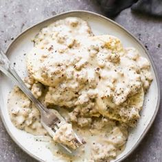 a white plate topped with meat covered in gravy and a fork next to it