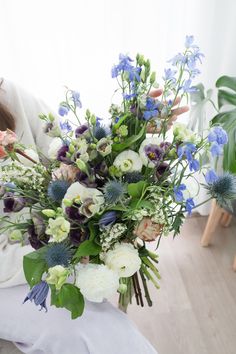 a woman holding a bouquet of flowers in her lap while sitting on the floor next to a window