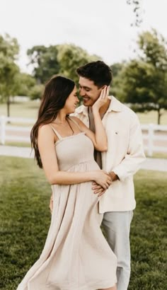 a man and woman standing next to each other in the grass with their arms around each other