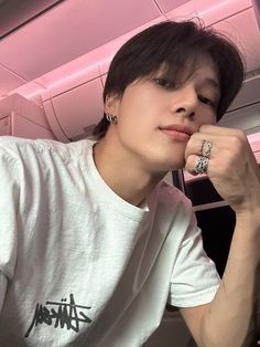 a young man wearing a white t - shirt and silver rings is sitting in an airplane