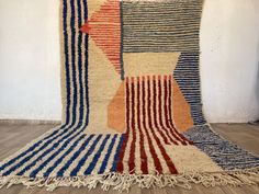 a multicolored area rug with fringes on the floor next to a white wall