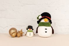 two crocheted snowmen with hats and scarves next to an acorn