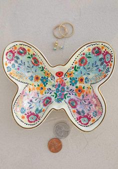 a butterfly shaped plate sitting on top of a table next to a coin and a keychain