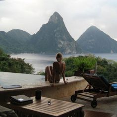 a woman sitting on the edge of a balcony looking out at water and mountains in the distance