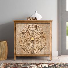 a wooden cabinet sitting on top of a floor next to a rug and vase in front of a window